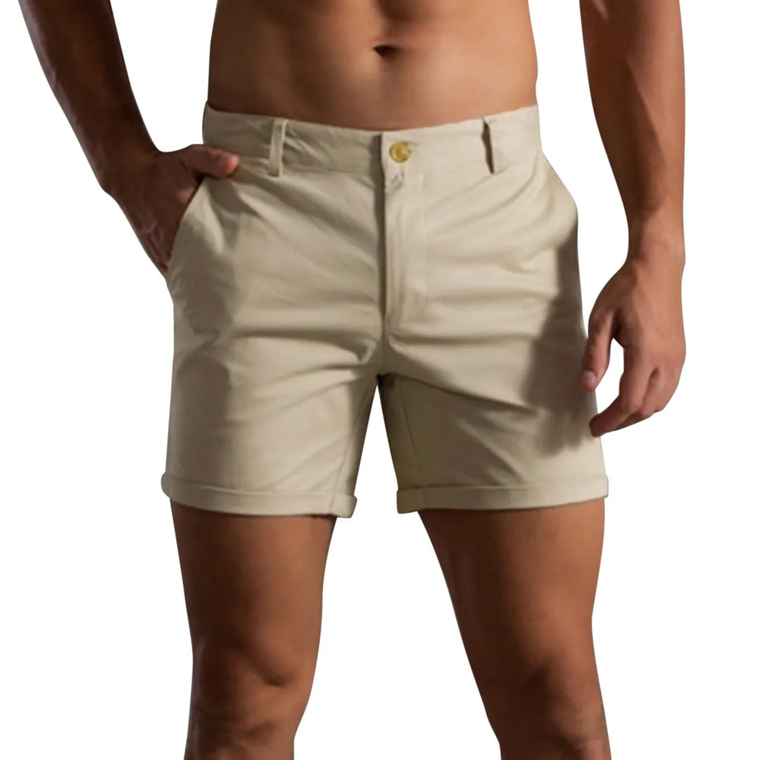 A person wearing light beige shorts with a tailored fit, rolled cuffs, belt loops, and a button closure, posing with one hand in their pocket against a plain white background.