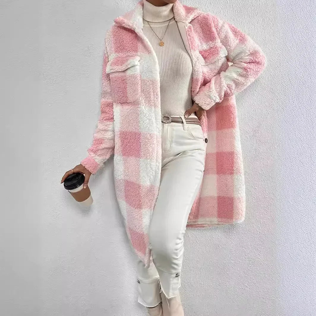 A person wearing a long, pink and white plaid Sherpa fuzzy coat with an open lapel over a white turtleneck sweater, white pants, and beige boots, holding a coffee cup and standing against a light-colored wall.