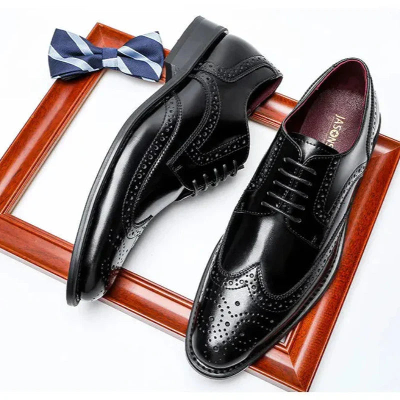 A pair of shiny premium leather brogue dress shoes with a cushioned insole is placed on a wooden picture frame, with a blue and white patterned bowtie beside them.