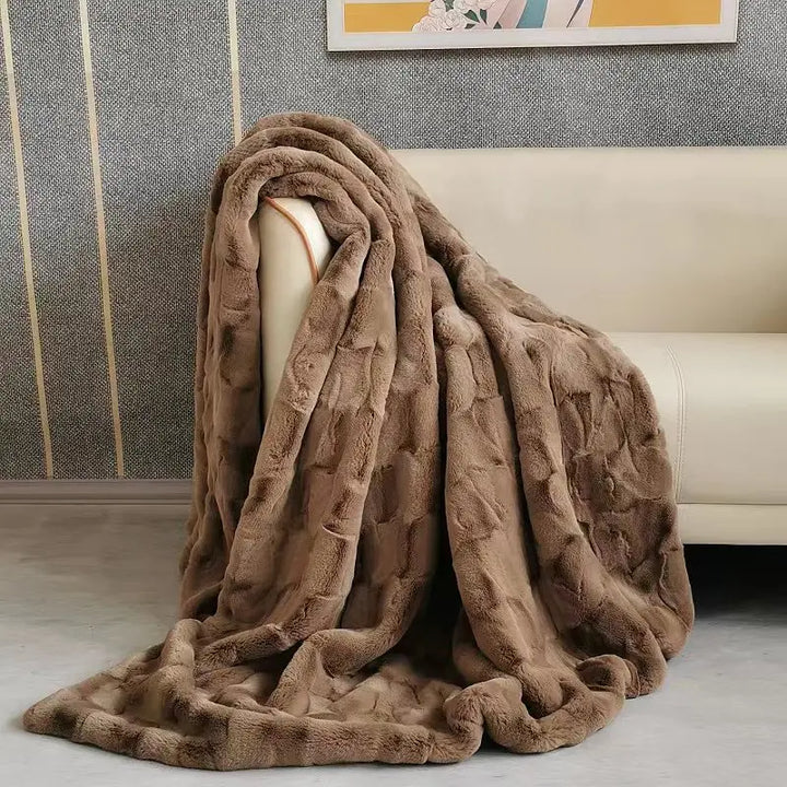 A plush faux fur blanket in rich brown drapes over the arm of a beige sofa in a modern living room with textured gray walls and a decorative framed picture above.