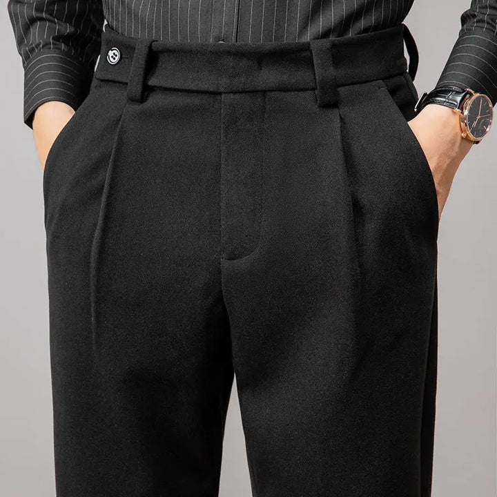 A person wearing tailored slacks and a black pinstripe shirt stands with hands in pockets; a wristwatch is visible on their left wrist.