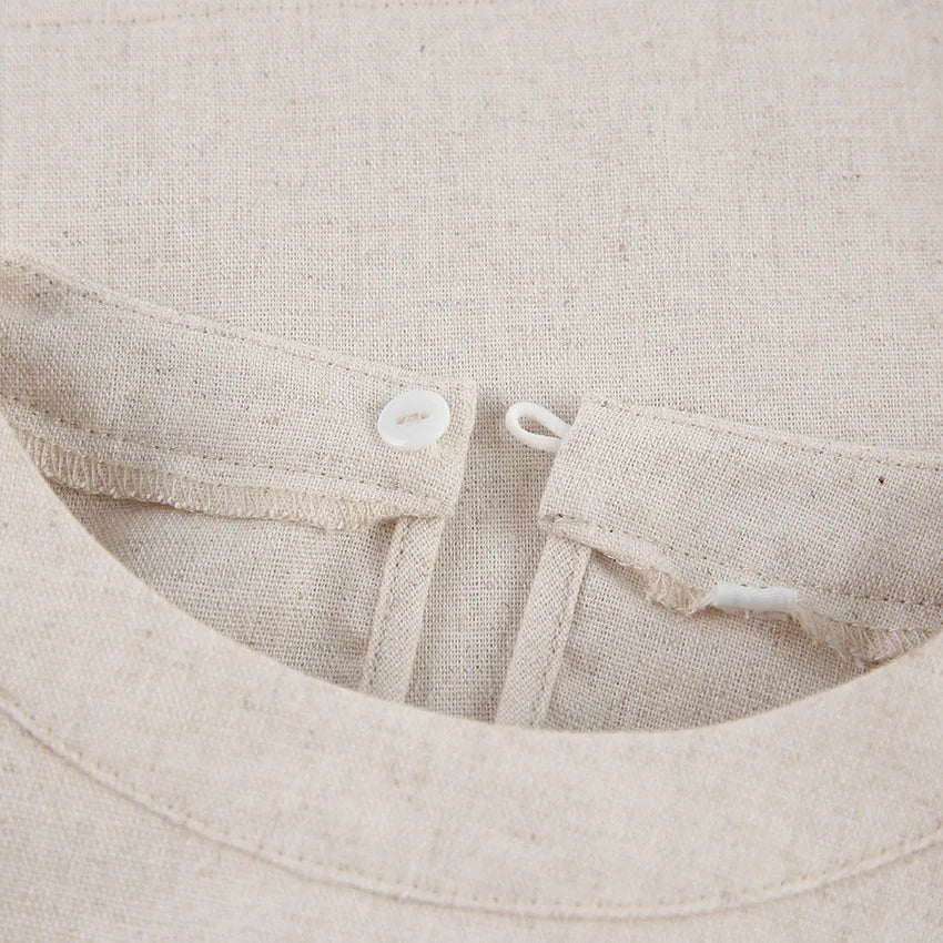 Close-up of a beige Belgian Linen Blend garment, showing a button loop closure at the neckline. The white button and natural, textured fabric highlight its refined design.