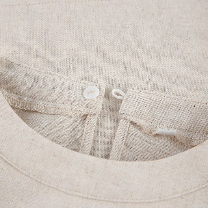 Close-up of a beige Belgian Linen Blend garment, showing a button loop closure at the neckline. The white button and natural, textured fabric highlight its refined design.