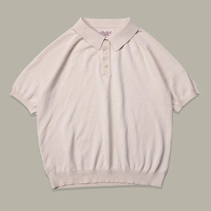 A beige mens polo shirt in classic style, crafted from soft organic cotton knit, features a collar, three buttons at the neck, and ribbed cuffs and hem, laid flat on a light gray background.