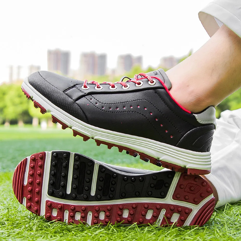 A person wearing black waterproof golf shoes with red accents and white soles stands on green grass, one foot atop the other, showing the shoe’s tread pattern. A city skyline is visible in the blurred background.