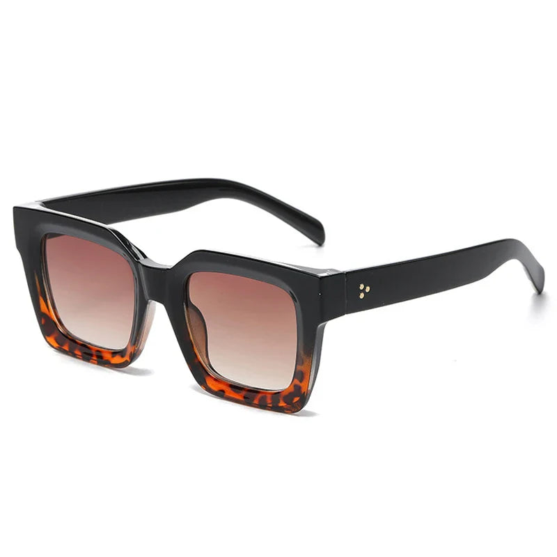 Square-framed sunglasses with thick black acetate frames, brown tortoiseshell detailing at the bottom, and gradient brown lenses. The temples are solid black with small gold dots near the hinges, offering stylish UV protection.