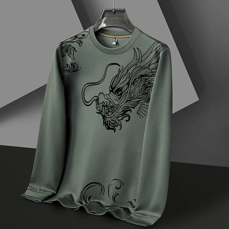 A green ultra-soft cotton crewneck with a large, detailed black dragon design on the front, displayed on a black hanger against a modern, geometric grey background.