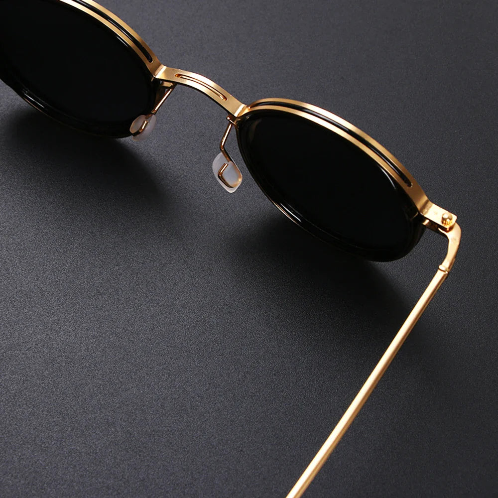 Close-up of stylish Ruby Ray Sunglasses with black polarized lenses and a shiny gold metal frame, resting on a dark, textured surface for ultimate UV400 protection.