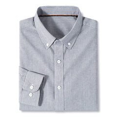 A classic pinstripe shirt, this neatly folded long-sleeve cotton button-up features thin vertical black and white stripes with white buttons, set against a plain white background.