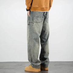 A person wearing a brown sweatshirt, classic fit stone washed jeans, and tan shoes stands with hands in pockets, facing away from the camera against a plain background.