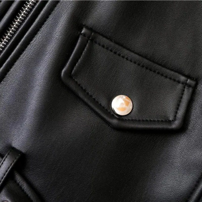 Close-up of a black leather jacket featuring a small flap pocket with a shiny metal snap button, part of a metal zipper on the left side, and detailing of an adjustable waist belt for a sleek, tailored fit.