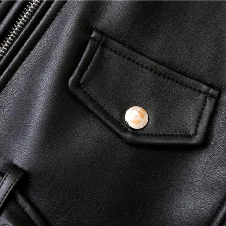 Close-up of a black leather jacket featuring a small flap pocket with a shiny metal snap button, part of a metal zipper on the left side, and detailing of an adjustable waist belt for a sleek, tailored fit.