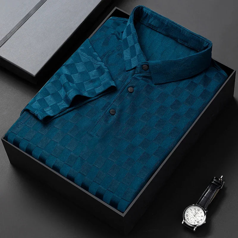 A dark teal, short-sleeve, tailored fit button-up shirt with a checkerboard pattern is neatly folded in a black gift box. A classic wristwatch with a black strap is placed nearby on a black surface.