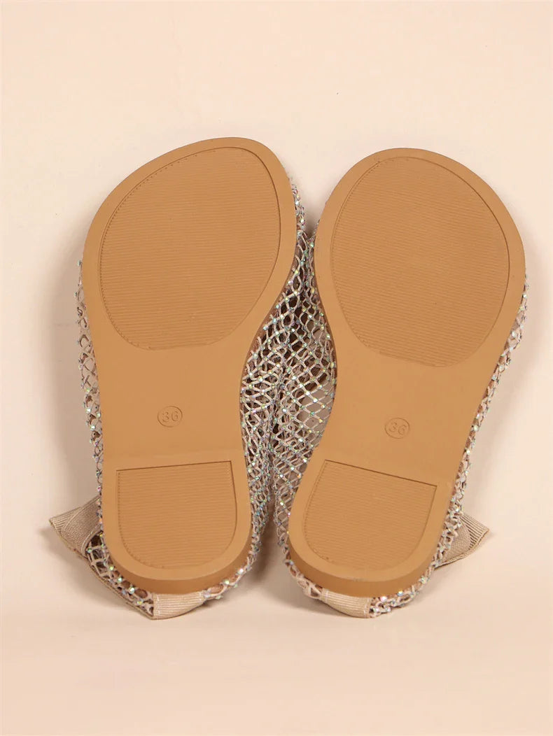 A pair of mesh overlay shoes is shown upside down, displaying their tan rubber soles and textured grip pattern. The shoes feature a sparkly upper design for added style.