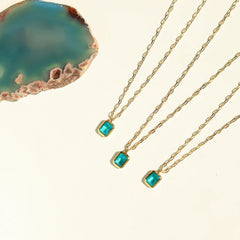 Three 18K gold plated necklaces with rectangular turquoise pendants are arranged diagonally on a cream background, next to a blue-green agate slice with brown edges. All pieces are hypoallergenic for comfortable everyday wear.