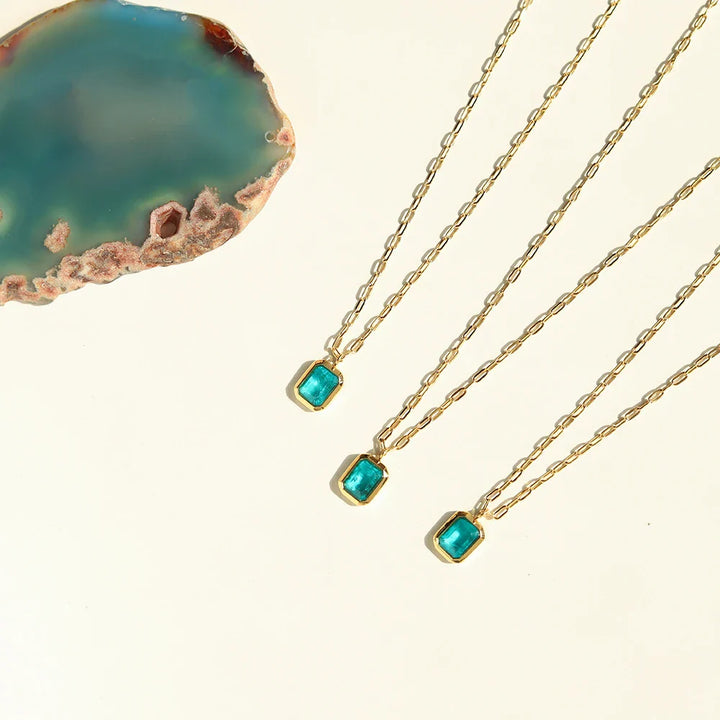 Three 18K gold plated necklaces with rectangular turquoise pendants are arranged diagonally on a cream background, next to a blue-green agate slice with brown edges. All pieces are hypoallergenic for comfortable everyday wear.