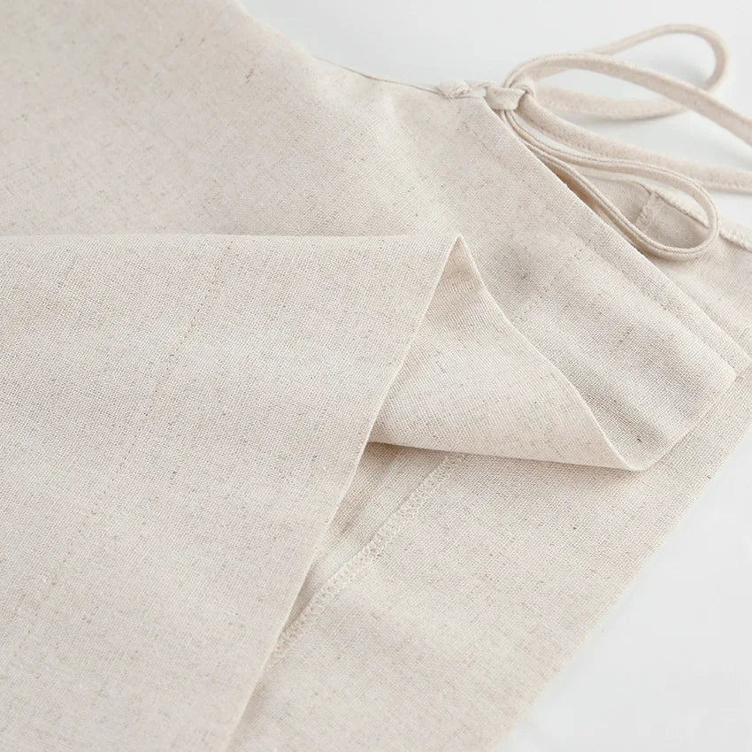 Close-up of beige Belgian Linen Blend fabric folded neatly, showing a stitched seam and drawstring ties, likely part of a garment such as wide-leg pants or an apron, on a white background.