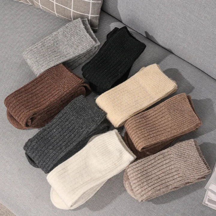 Nine pairs of ribbed knit socks in various neutral colors, crafted from a cashmere cotton blend for superior insulation, are neatly arranged on a light gray fabric surface.