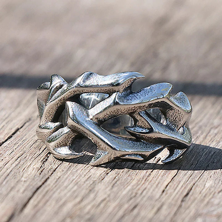 A silver streetwear ring with a rugged, intertwined branch or antler design rests on a weathered wooden surface—an edgy piece perfect for fashion jewelry lovers.