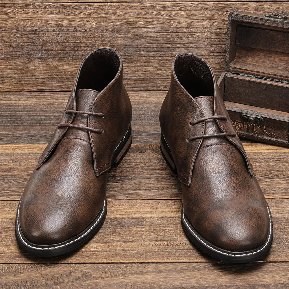 A pair of brown After-Ride Chukka leather boots with black soles and white stitching, placed on a wooden surface next to an open wooden box, showcasing their Western-inspired chukka design.