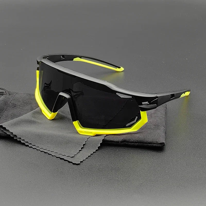 Sporty black Olympus Sunglasses with yellow accents rest on a gray cleaning cloth and black pouch, displayed on a dark surface. The large, mirrored lenses offer UV protection in a modern, angular design.