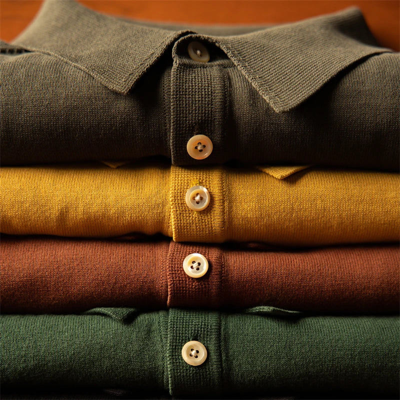 A neatly folded stack of four men’s polo shirts in olive green, yellow, brown, and dark green, each featuring a classic style polo design with buttons visible down the front.