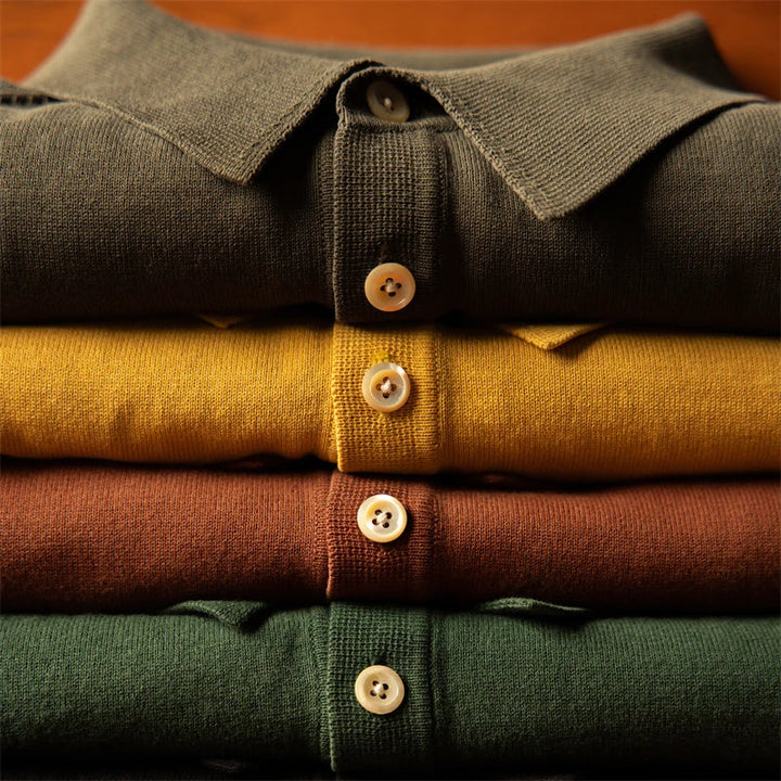 A neatly folded stack of four men’s polo shirts in olive green, yellow, brown, and dark green, each featuring a classic style polo design with buttons visible down the front.