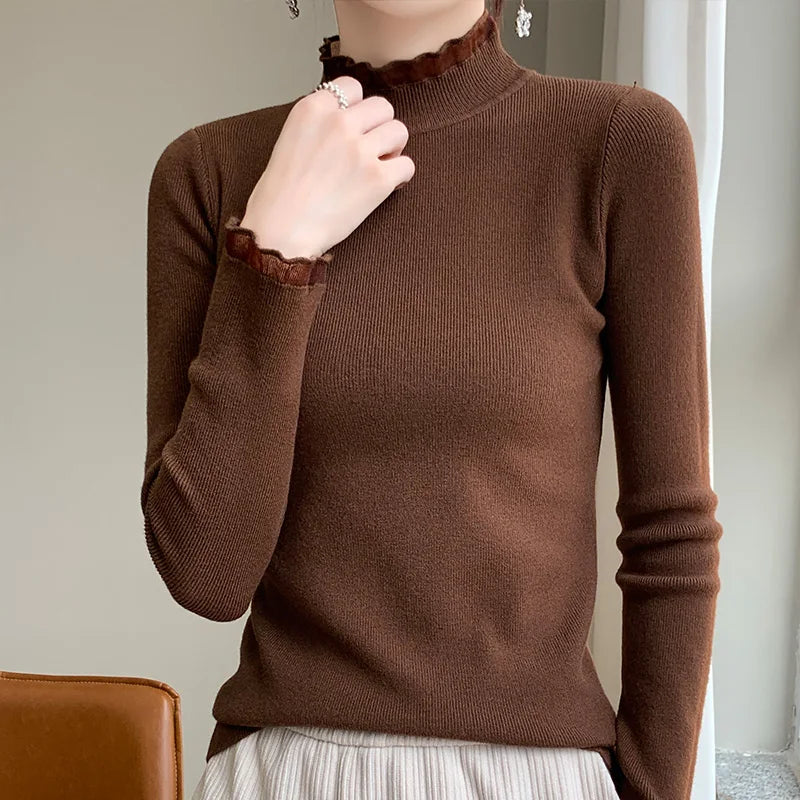 A person wearing a fitted brown cashmere blend long-sleeve sweater with ruffled mock neck and cuffs, paired with a light-colored pleated skirt, is seated indoors. The face is not visible.
