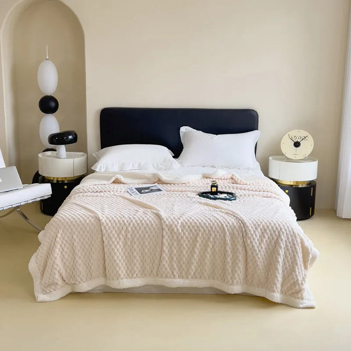 A modern bedroom with a black headboard bed, white pillows, an ultra-soft cotton blanket, circular nightstands with decor, and a white chair with a laptop. The room features minimalist, neutral-toned decor.