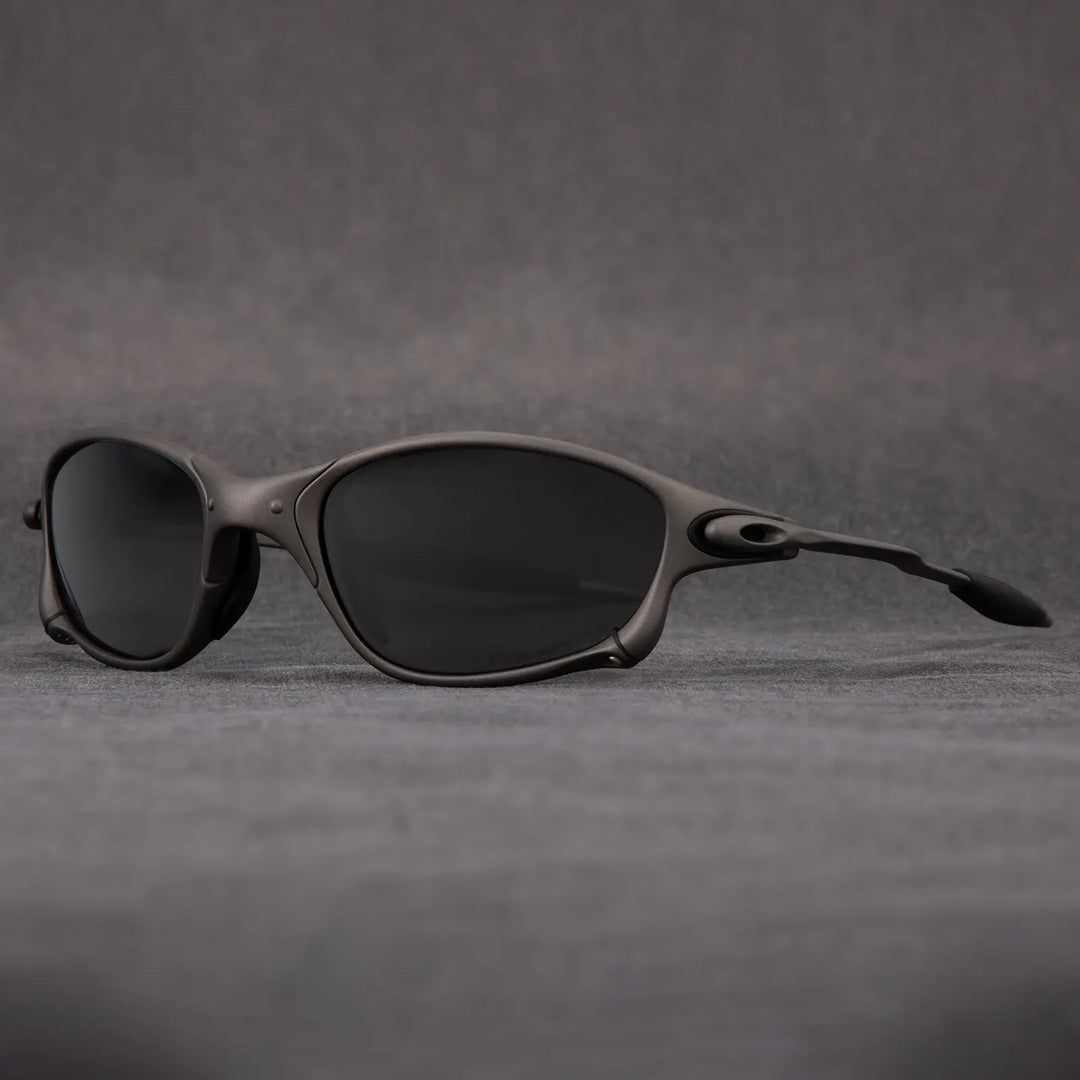 A pair of black, oval-shaped polarized sunglasses with a sleek, matte frame is displayed on a gray surface against a gray background, offering stylish outdoor eyewear with UV protection.