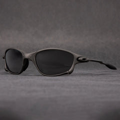A pair of black, oval-shaped polarized sunglasses with a sleek, matte frame is displayed on a gray surface against a gray background, offering stylish outdoor eyewear with UV protection.