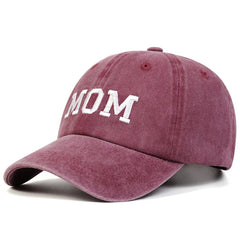 A pink vintage streetwear Mom & Dad cap with the word MOM embroidered in white capital letters on the front.