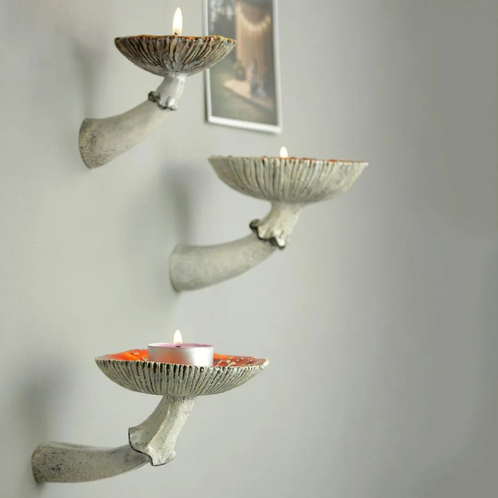 Three decorative wall-mounted candle holders shaped like stylized animal horns add unique home decor flair, each holding a lit tealight and arranged vertically on a light-colored wall, with a framed picture in the background.