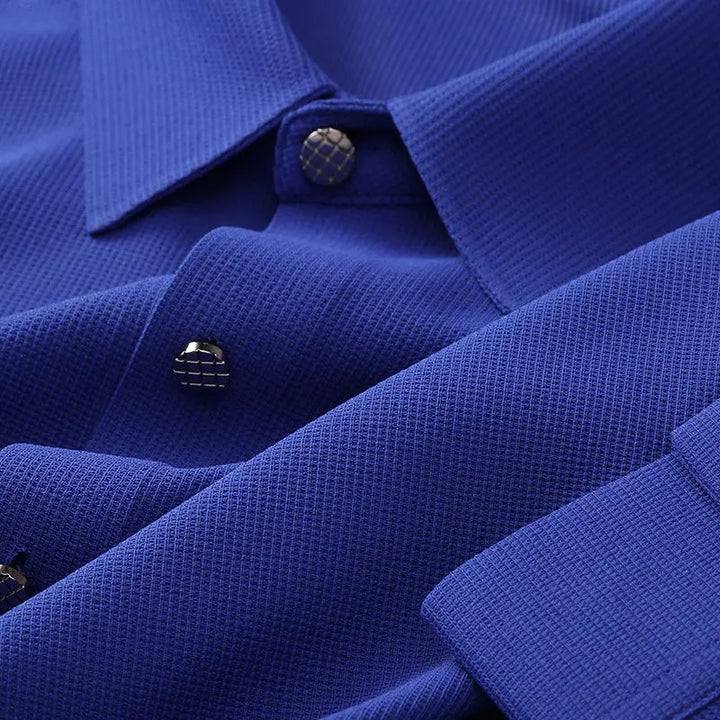 Close-up of a blue wrinkle-resistant shirt showing the collar, metallic grid-patterned buttons, and fabric texture. The shirt appears neatly pressed and stylish.