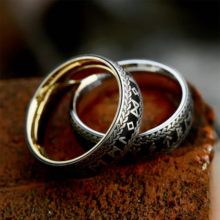 Two silver Viking Rune Rings with intricate engraved designs and gold interiors rest on a textured, reddish-brown brick surface. The couple's amulet rings feature patterns and symbols reminiscent of ancient or fantasy scripts.