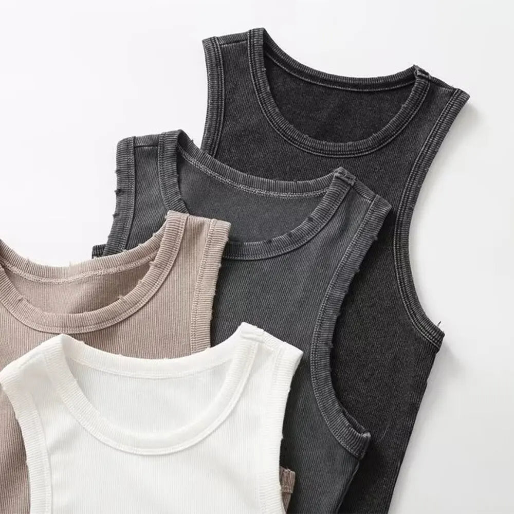 Four women’s tank tops in a water wash rib fabric—white, beige, gray, and black—are neatly stacked on a white background for a retro workwear-inspired look.