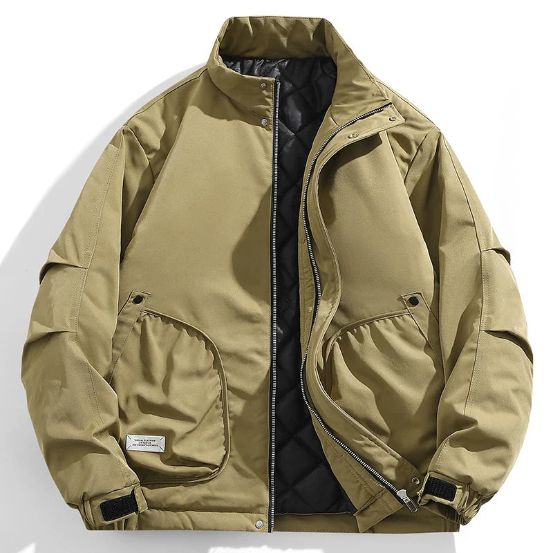A khaki green windproof jacket with a high collar, front zipper, two large flap pockets, adjustable cuffs, and a quilted inner lining, laid flat on a white background.