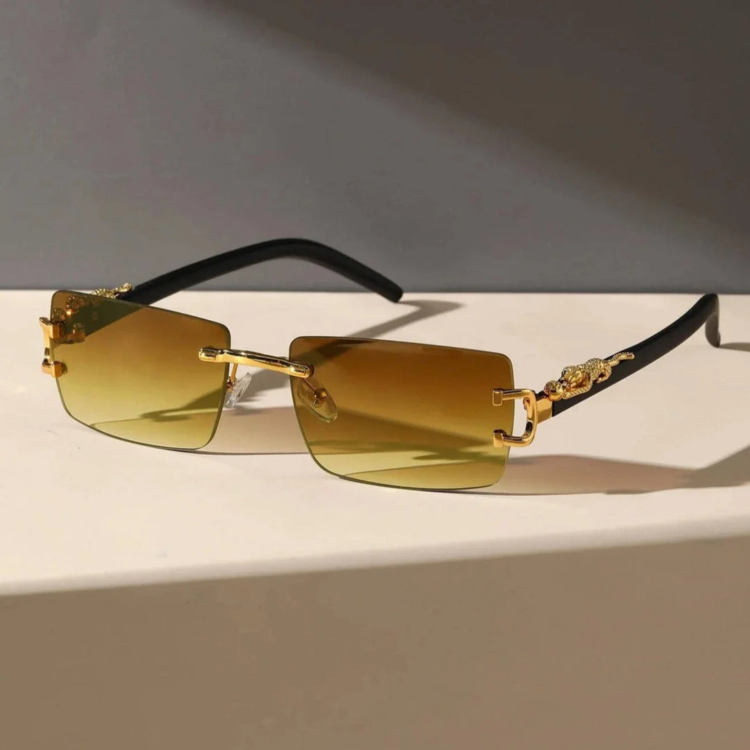 Brown rectangular rimless sunglasses with gold detailing on the temples and black arms, featuring durable hinges, displayed on a light-colored surface with a gray background.