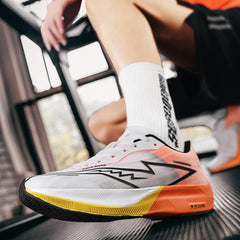 A close-up of a person wearing white, orange, and yellow running shoes with a bold lightning bolt design and shock-absorbing sole, paired with white socks. The person is in an indoor gym setting, kneeling by a window.