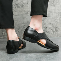 A person wearing low profile loafers with cutout sides and black pants stands on a concrete floor against a textured gray wall.