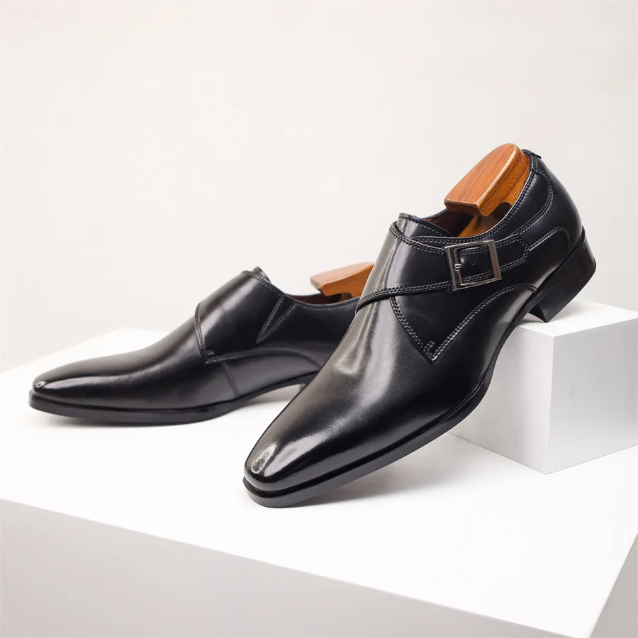 A pair of shiny black Italian leather monk strap shoes with a single buckle, displayed on a white surface with wooden shoe trees inside each shoe.