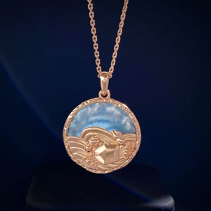 A gold pendant necklace featuring a round charm with a raised sailing boat on wavy water against a blue sky background, set on a simple gold chain with subtle astrology jewelry inspiration.