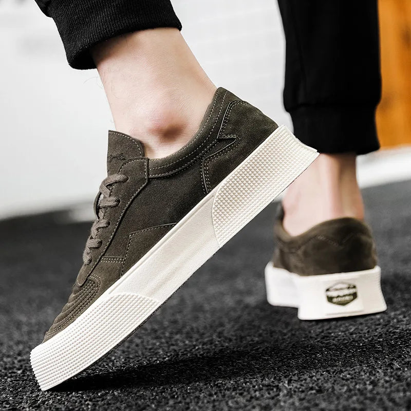 A person wearing olive green lace-up sneakers with thick white textured soles and comfortable cushioning is walking on a black carpeted surface. The pants are black and the background is blurred.