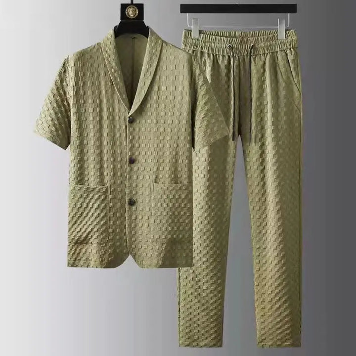 A matching light olive green two-piece set featuring a short-sleeve button-up shirt and pants with an elastic drawstring waistband, crafted from ultra-soft fabric with a textured, checkered pattern, displayed on hangers against a gray gradient background.
