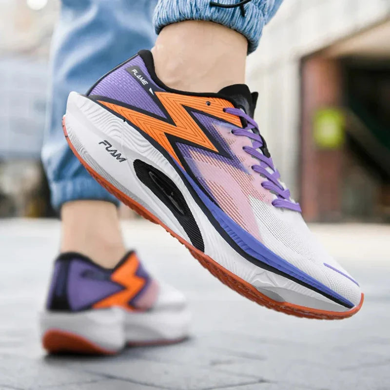 A person wearing colorful running shoes with purple, orange, black, and white accents walks on a paved street. Featuring a bold zigzag design and shock-absorbing sole, the shoes pair effortlessly with light blue jeans.
