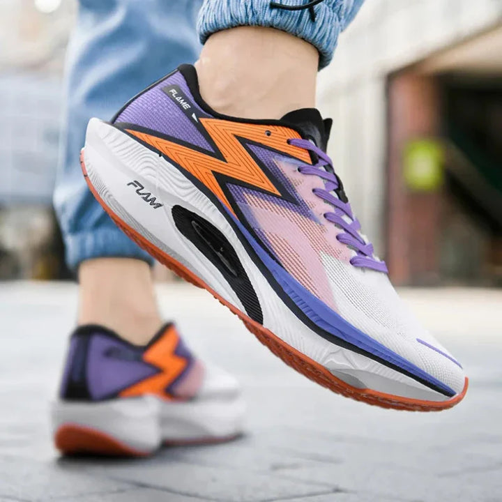 A person wearing colorful running shoes with purple, orange, black, and white accents walks on a paved street. Featuring a bold zigzag design and shock-absorbing sole, the shoes pair effortlessly with light blue jeans.