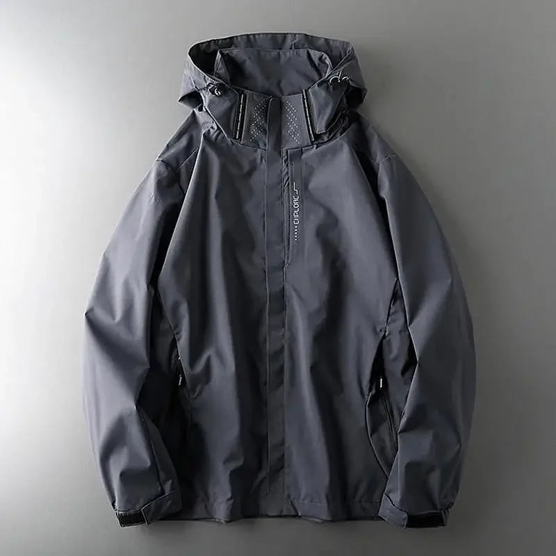 A dark gray breathable outdoor jacket with a hood is laid flat on a gray surface, showing the front side with a zipper closure and two side pockets.