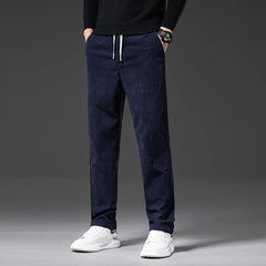 A person wearing navy blue men's smart casual pants with a drawstring, a black sweater, white sneakers, and a watch stands against a plain dark background. The photo is cropped at the shoulders, showing only the lower body.