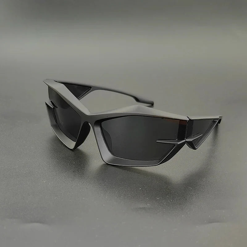 Angular, futuristic black sunglasses with geometric frames and high-contrast lenses rest on a smooth, dark surface against a simple, gray background.
