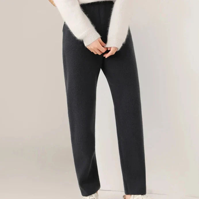 Person wearing a white fuzzy sweater and black straight-leg pants with a slim tailored leg, standing against a plain light-colored background. Their hands are clasped in front, and only the lower half of their body is visible.